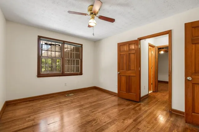 an empty room with wooden floor chandelier fan and windows