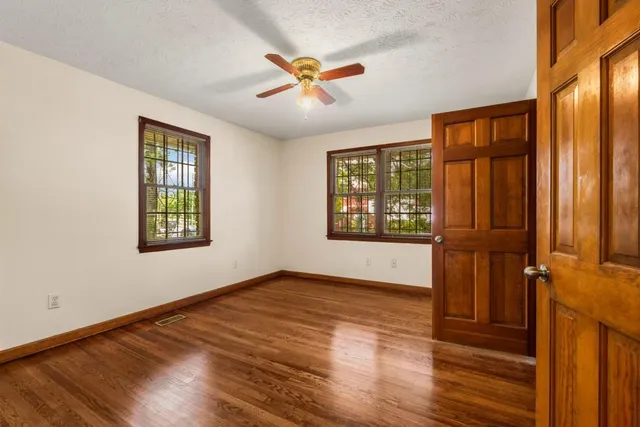 an empty room with wooden floor fan and windows