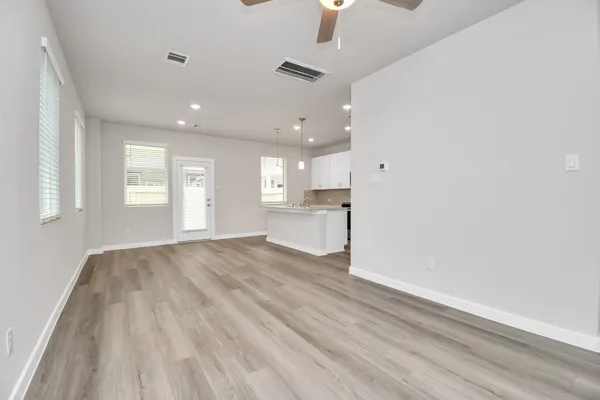 an empty room with wooden floor kitchen view and windows