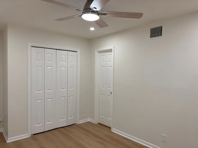 an empty room with a chandelier fan and wooden floor