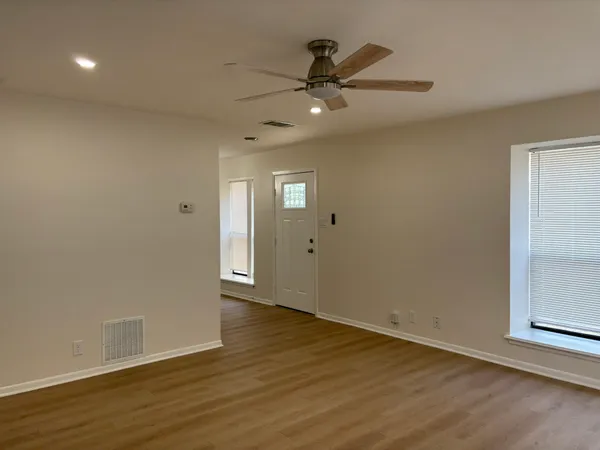 an empty room with wooden floor fan and windows