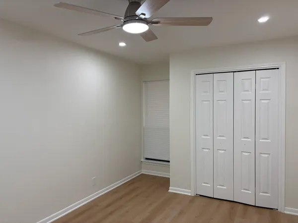 an empty room with wooden floor fan and windows