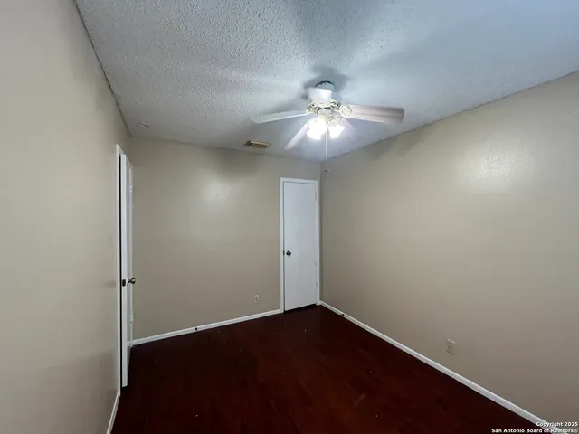 an empty room with a chandelier fan and wooden floor