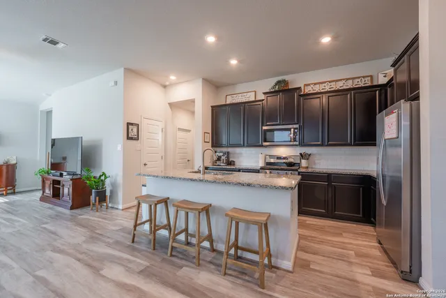 a kitchen with stainless steel appliances granite countertop a refrigerator a stove top oven a sink dishwasher and white cabinets with wooden floor