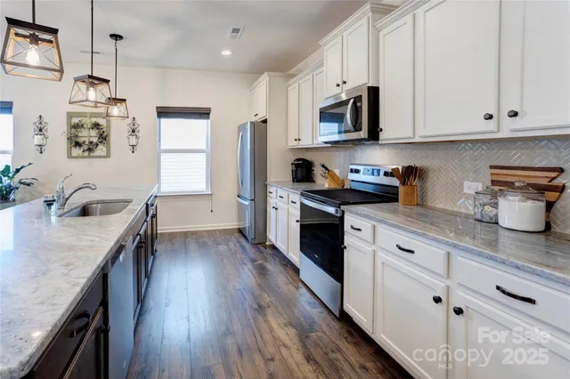 a kitchen with granite countertop a sink dishwasher stove and white cabinets with wooden floor