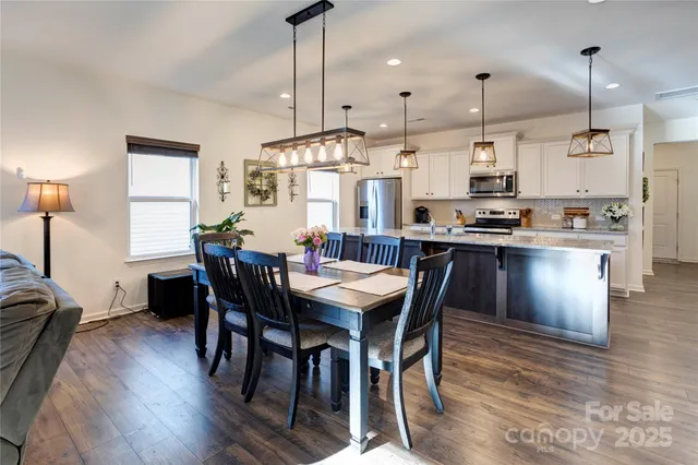 a view of kitchen with stainless steel appliances kitchen island granite countertop dining table chairs and sink