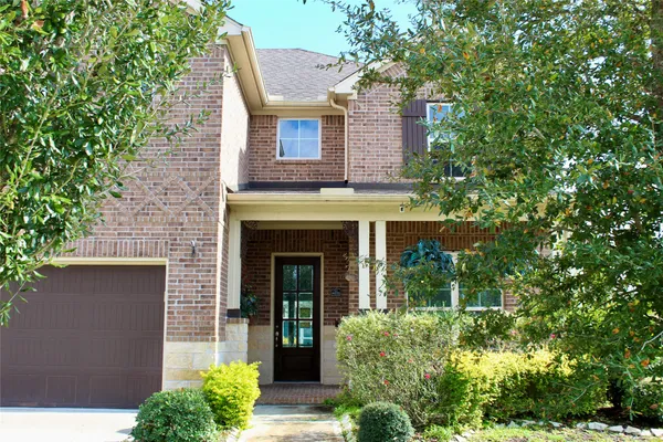 a view of a brick house with plants and large trees