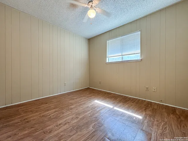 a view of an empty room with wooden floor and a chandelier fan