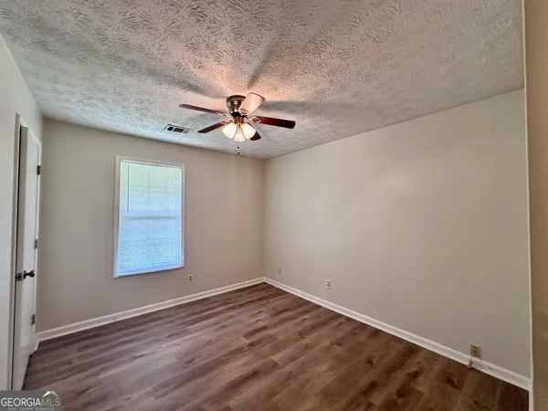 an empty room with a chandelier fan and wooden floor