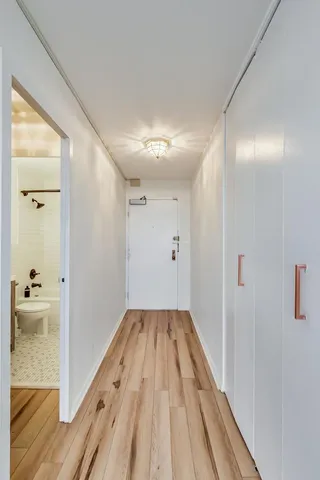 a view of a hallway with wooden floor and a bathroom