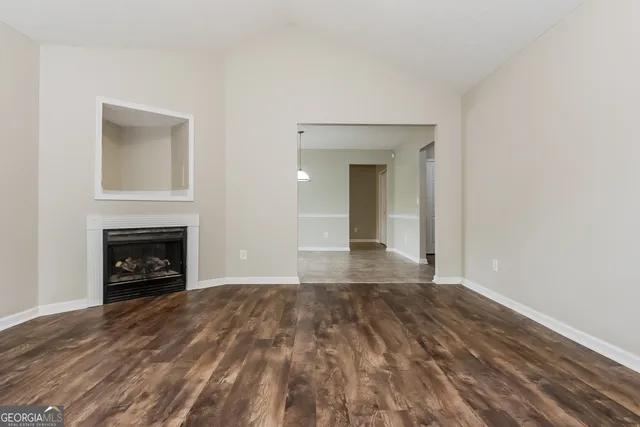 a view of an empty room with wooden floor fireplace and a window