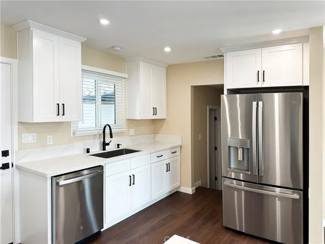 a kitchen with stainless steel appliances granite countertop a refrigerator a sink and white cabinets with wooden floor