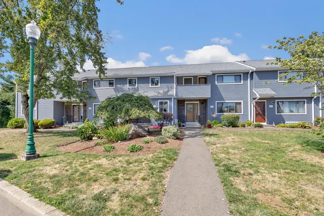 a view of a brick house with many windows plants and large tree