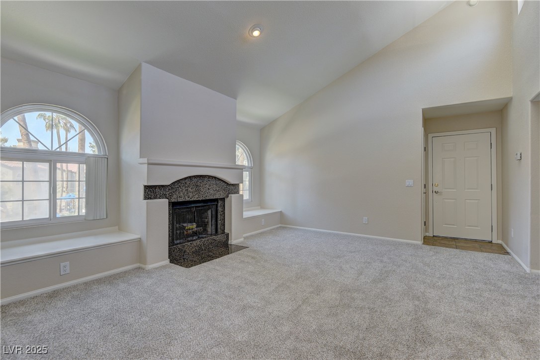 Unfurnished living room with carpet flooring, high vaulted ceiling, plenty of natural light, a fireplace, and baseboards