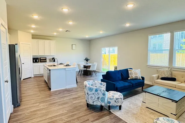 a living room with couches kitchen view and a refrigerator