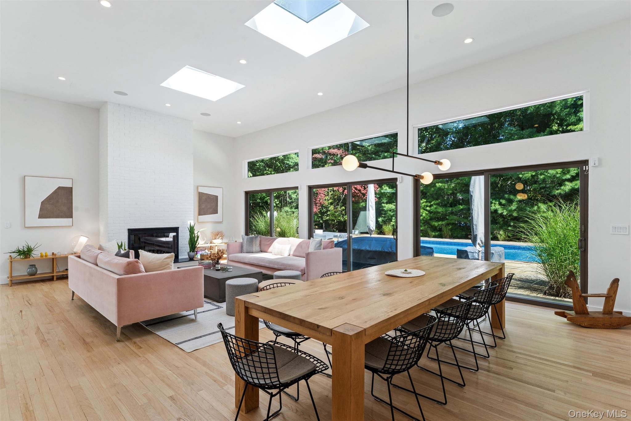 8 Deer Path Quogue, NY 11959 - Photo 4 of 23 Dining room featuring a towering ceiling, a brick fireplace, light wood finished floors, recessed lighting, and a skylight