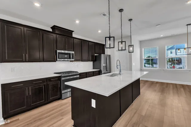 a large kitchen with kitchen island granite countertop a refrigerator a stove a sink and a oven with wooden floor