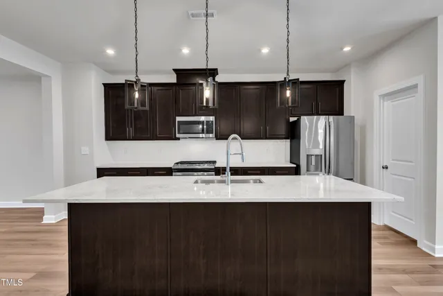 a kitchen with stainless steel appliances kitchen island granite countertop a stove a refrigerator a sink and dishwasher with wooden floor