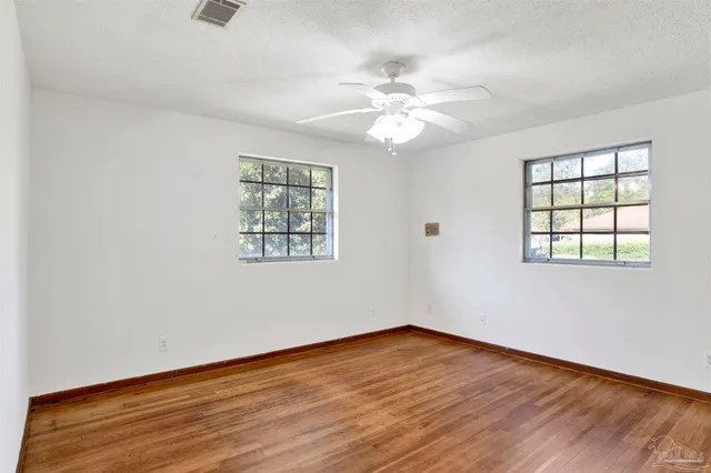 an empty room with wooden floor chandelier fan and windows
