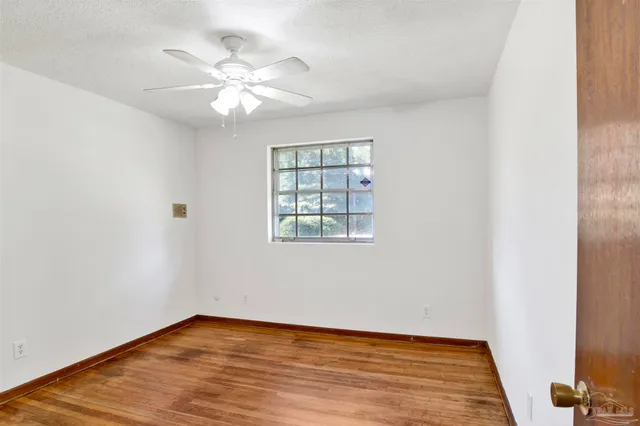 an empty room with wooden floor chandelier fan and windows