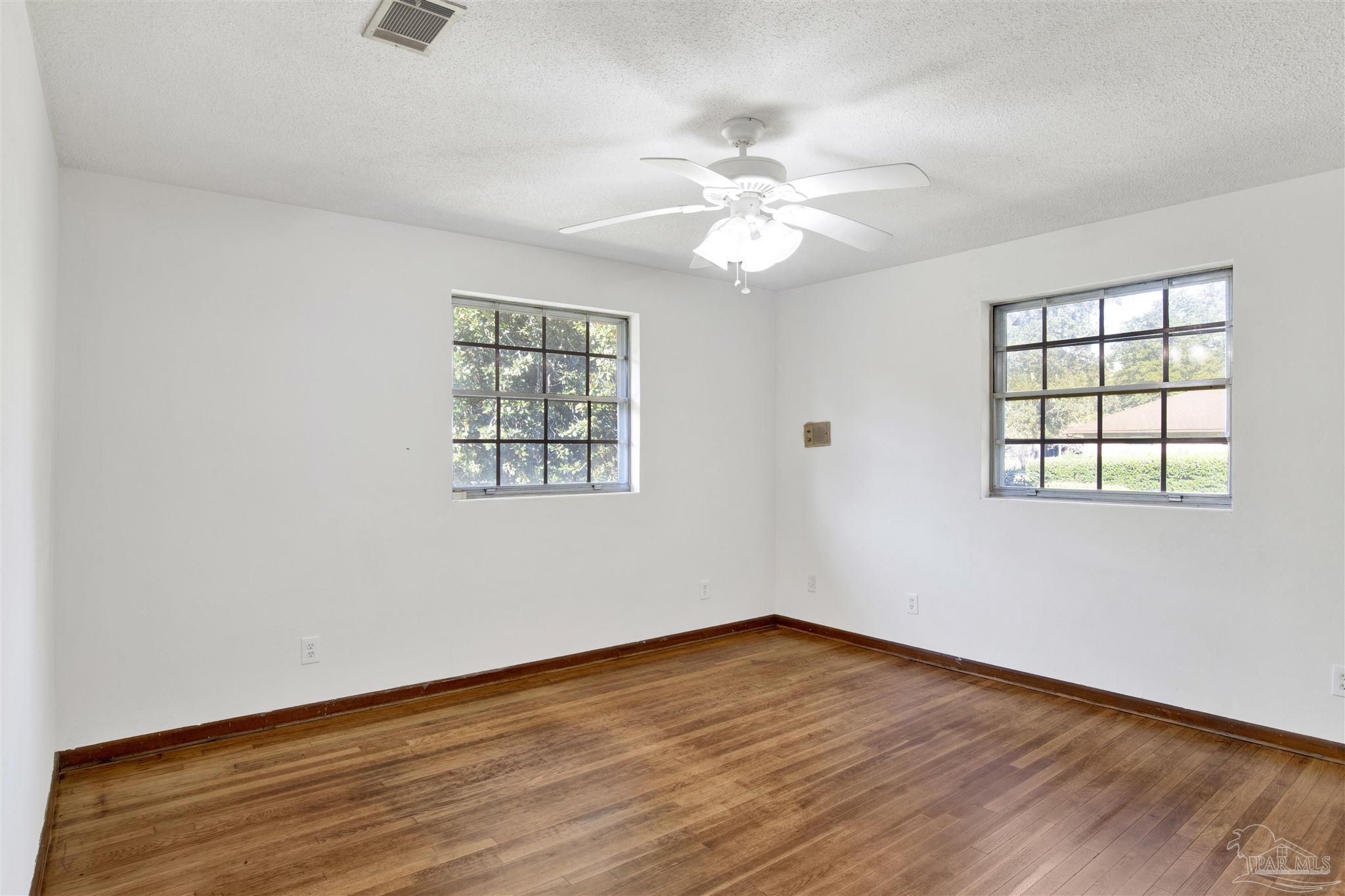 9621 Sidney Road Pensacola, FL 32507 - Photo 17 of 30 an empty room with wooden floor chandelier fan and windows