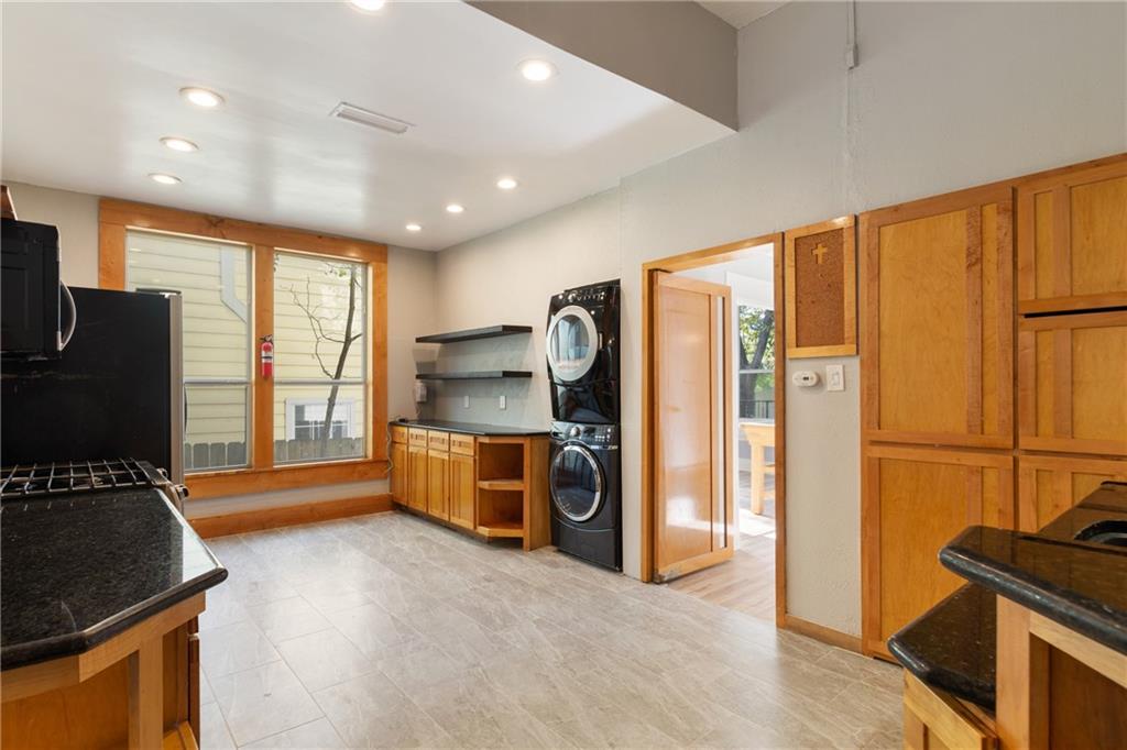 3210 Hampton Road, Unit A B C Austin, TX 78705 - Photo 39 of 42 Kitchen area featuring granite countertops, wood-finish cabinetry, integrated stacked laundry appliances, recessed lighting, and large windows with natural wood trim
