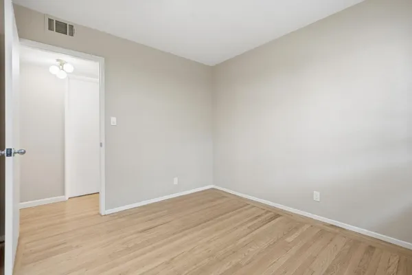 a view of an empty room with wooden floor and a bathroom