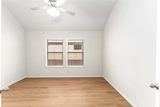 an empty room with wooden floor fan and windows
