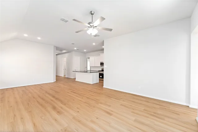 a view of an empty room with wooden floor and a ceiling fan