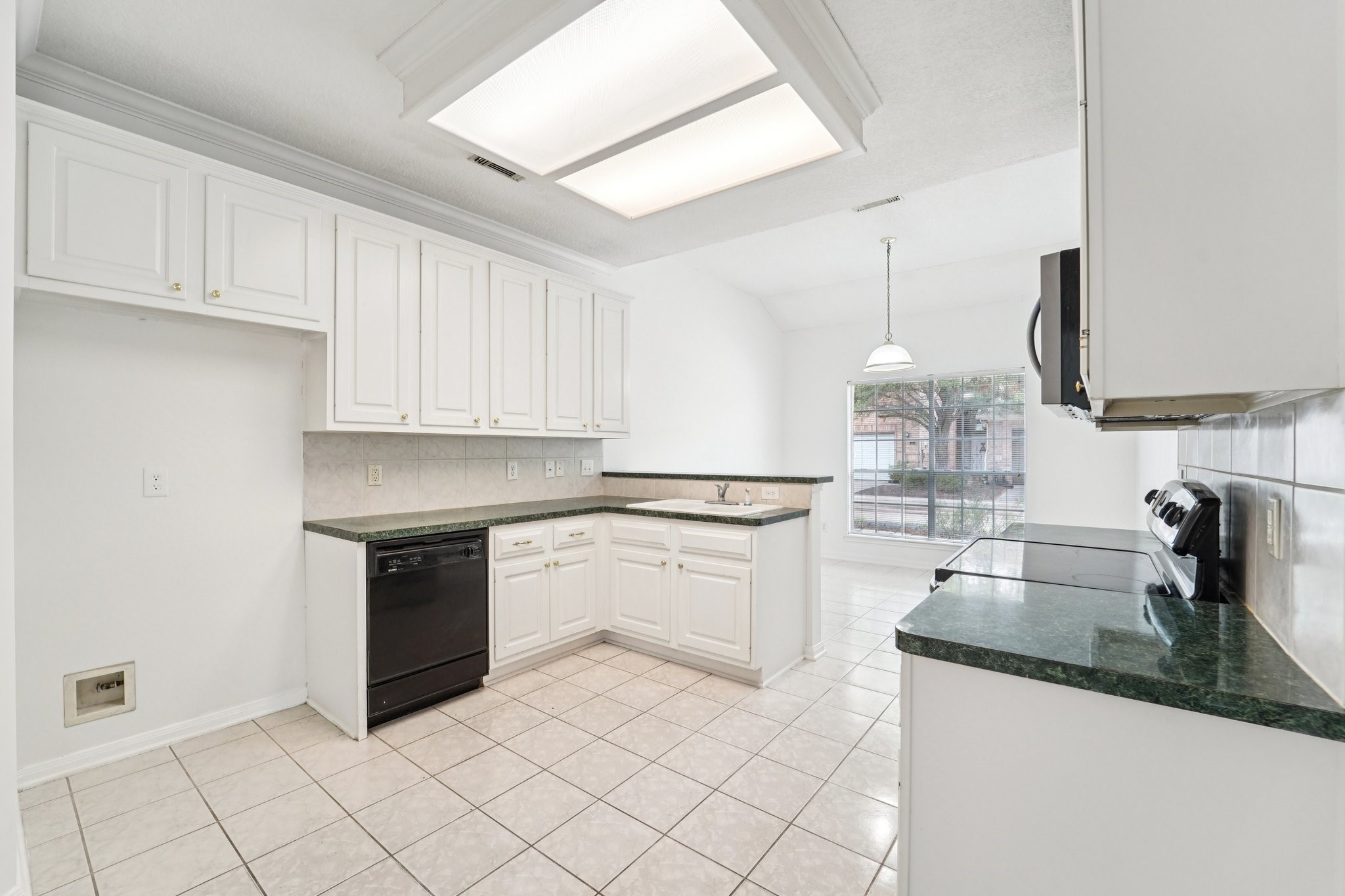 14420 Walters Road, Unit 55 Houston, TX 77014 - Photo 14 of 35 Bright and spacious kitchen with white cabinetry, dark countertops, and tiled flooring. It includes a dishwasher, oven, and a large window for natural light, leading to a dining nook with a pendant light.