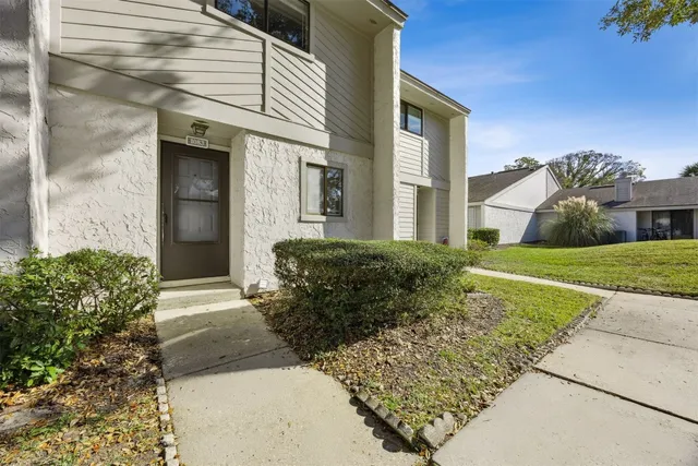 a view of a house with brick walls plants and large tree
