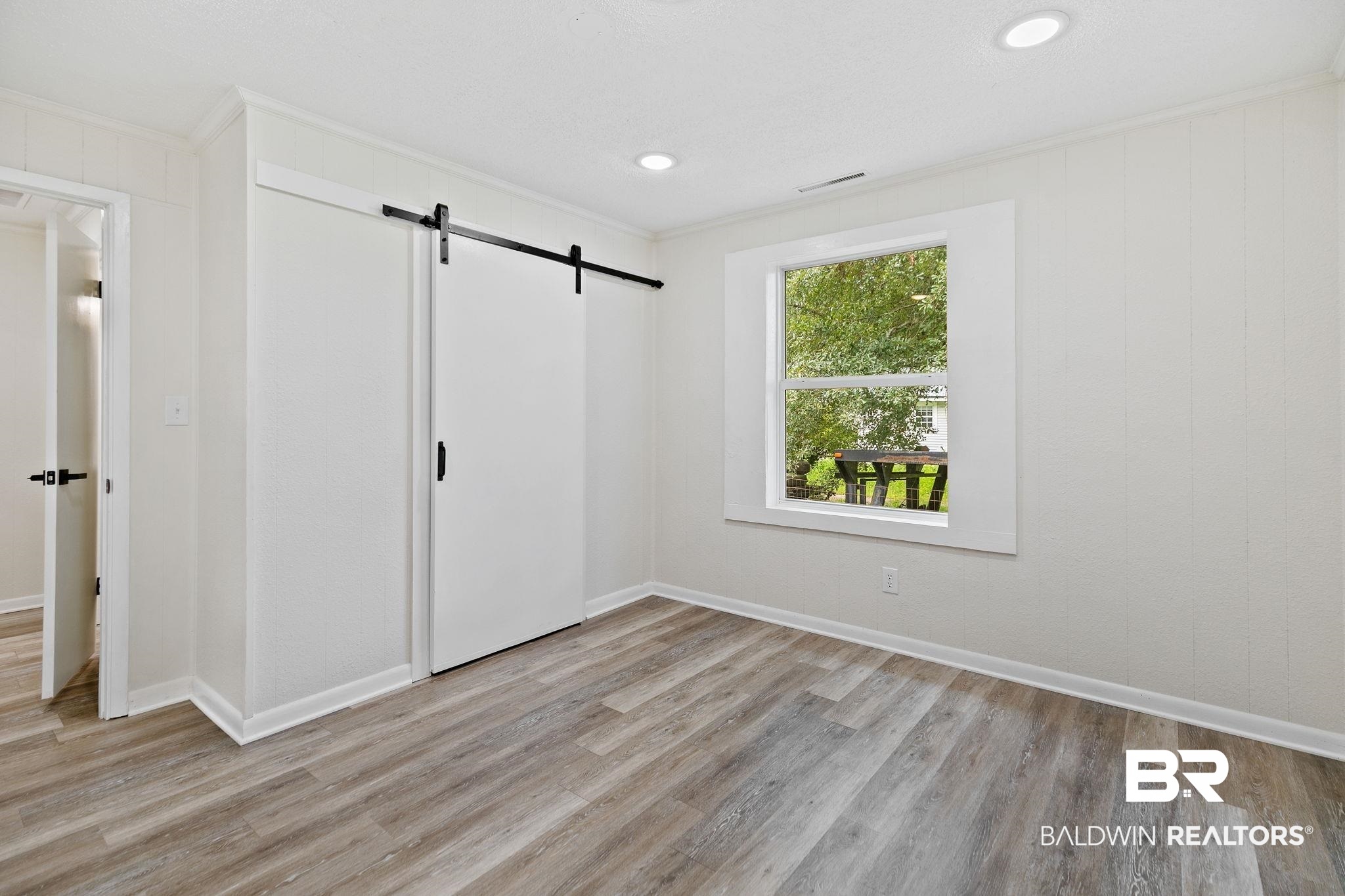 507 Byrne Street Bay Minette, AL 36507 - Photo 30 of 40 Unfurnished bedroom featuring a barn door, ornamental molding, a closet, and light hardwood / wood-style floors