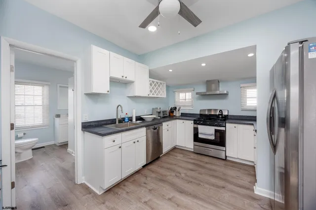 a kitchen with stainless steel appliances granite countertop a stove top oven a sink a refrigerator and white cabinets with wooden floor