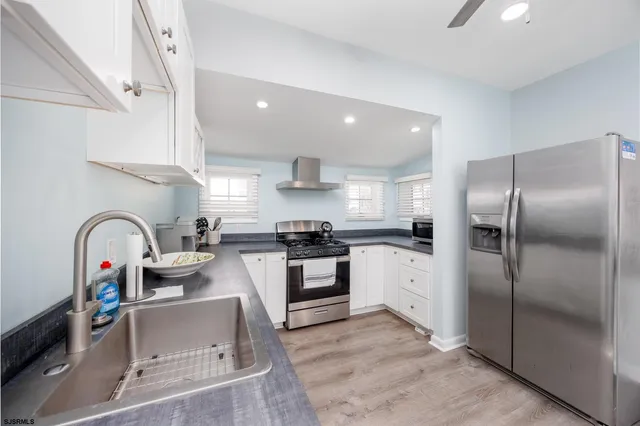 a kitchen with stainless steel appliances granite countertop a refrigerator a sink a stove and white cabinets