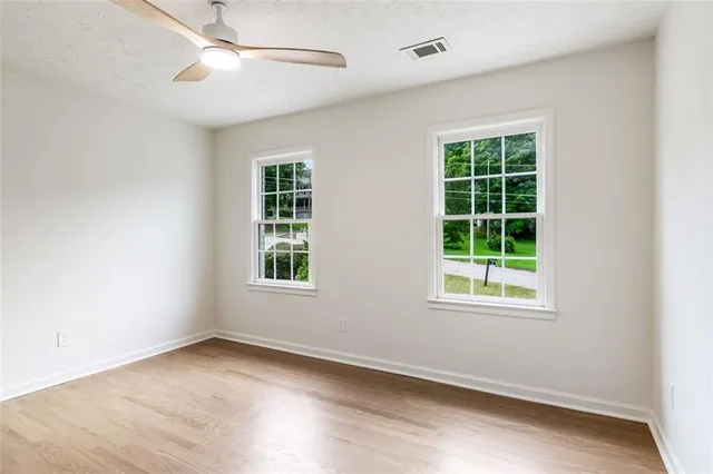 an empty room with wooden floor chandelier fan and windows