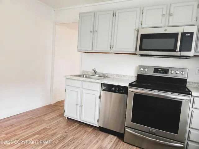 a kitchen with stainless steel appliances a stove a microwave oven cabinets and a wooden floor