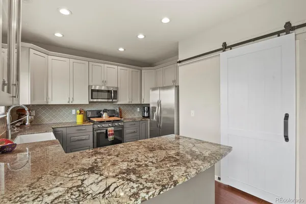 a kitchen with granite countertop a refrigerator sink stove and white cabinets