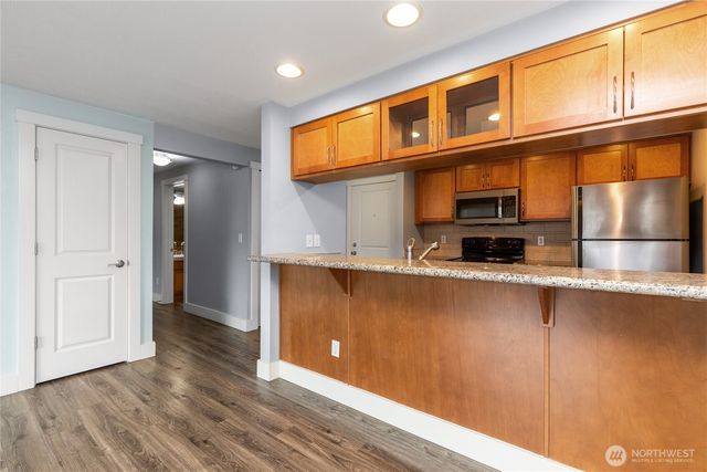a view of kitchen with stainless steel appliances granite countertop a refrigerator a stove and a wooden floors