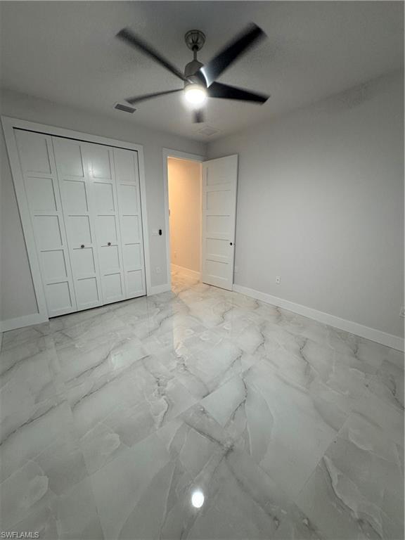 2963 18th Avenue Northeast Naples, FL 34120 - Photo 7 of 10 Unfurnished bedroom with light marble finish flooring, a closet, and a ceiling fan