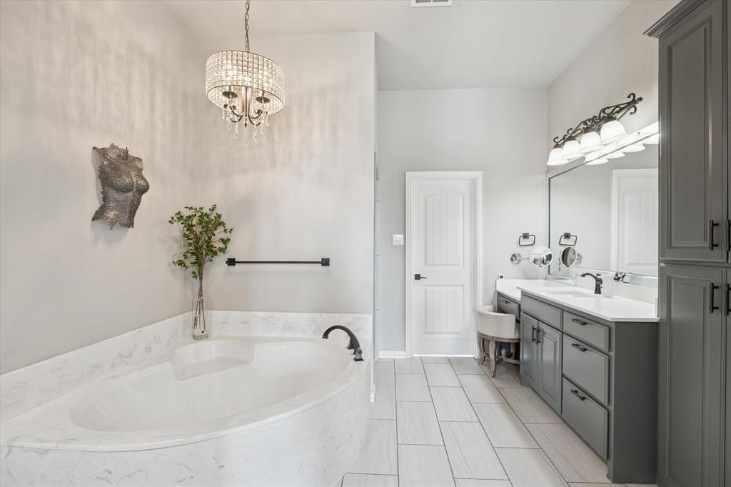 542 Pierce Road Red Oak, TX 75154 - Photo 15 of 27 Bright bathroom featuring a built-in tub with a stone-finish surround, a crystal chandelier, and plank-style tile flooring