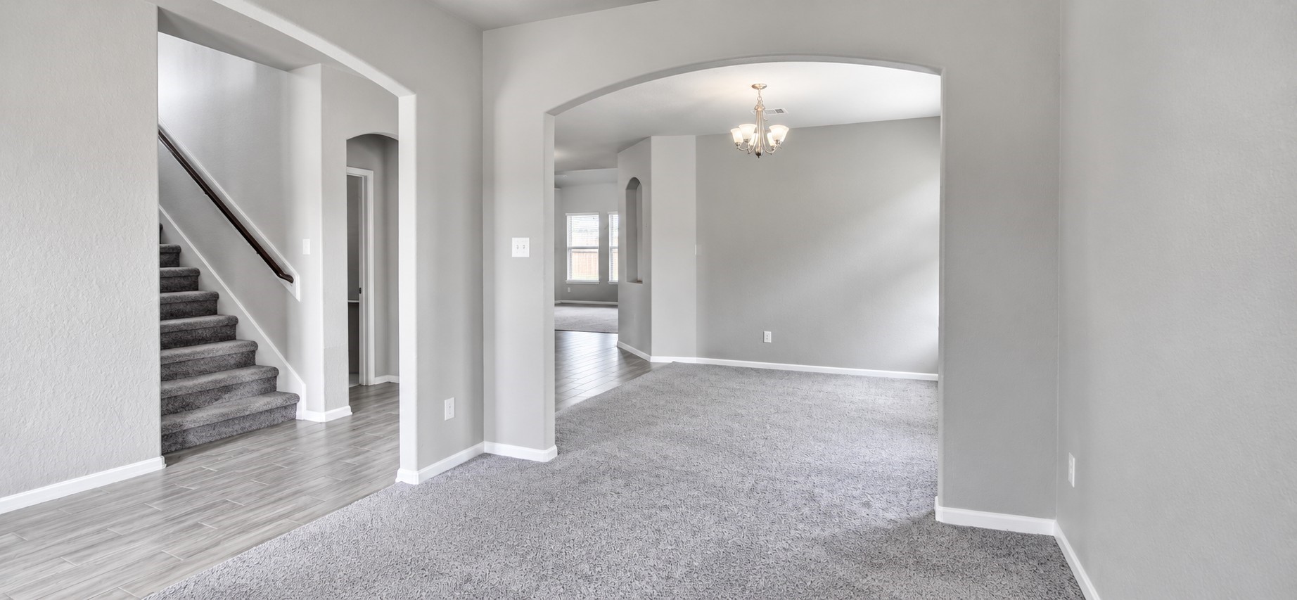 11355 Cascading Stream Way Houston, TX 77044 - Photo 3 of 17 Spacious and inviting living area with fresh gray carpeting, modern light fixtures, and an elegant arched entryway leading to a cozy dining space.