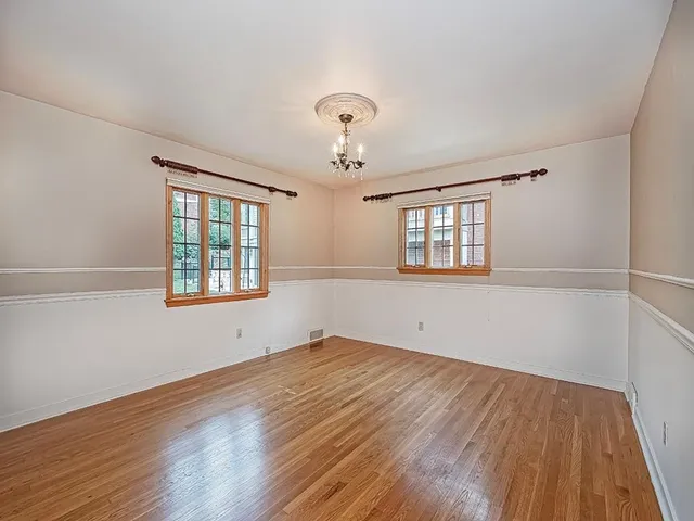 an empty room with wooden floor chandelier and windows