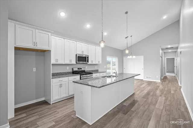 a kitchen with stainless steel appliances kitchen island granite countertop a stove a sink and white cabinets with wooden floor