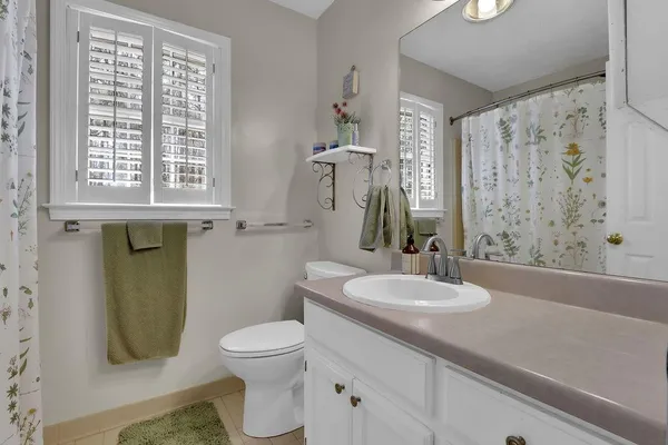 a bathroom with a granite countertop toilet a sink a mirror a window and a shower