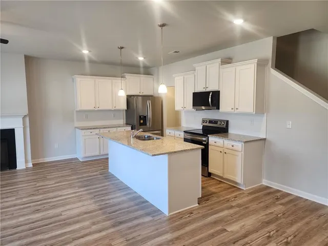 a kitchen with stainless steel appliances granite countertop a stove top oven a refrigerator a sink and dishwasher with wooden floor