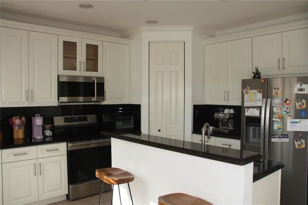 a kitchen with stainless steel appliances kitchen island granite countertop a refrigerator a stove a sink and white cabinets with wooden floor