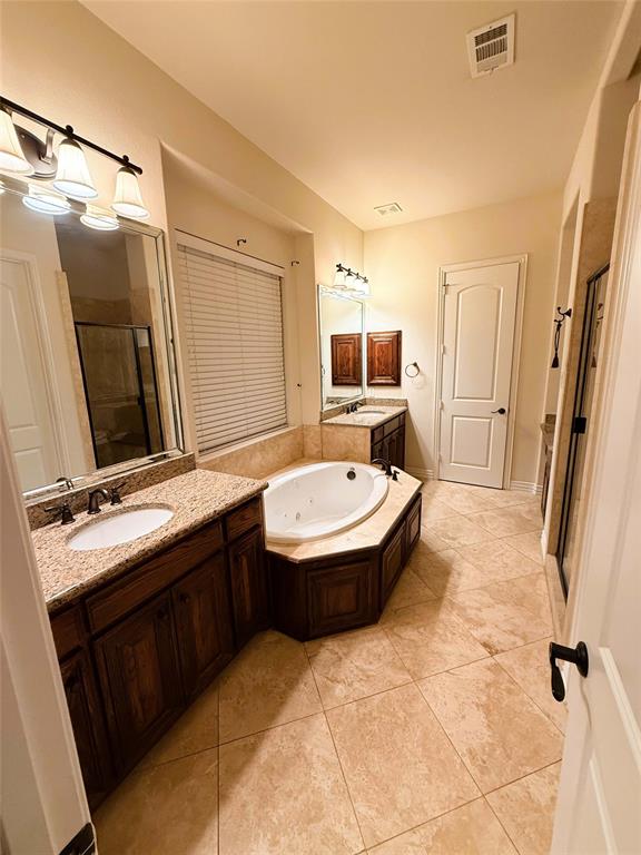 2215 Longview Road Irving, TX 75063 - Photo 13 of 25 Spacious bathroom featuring a built-in jetted tub, dual vanity sinks with granite countertops, rich wood cabinetry, and neutral tile flooring