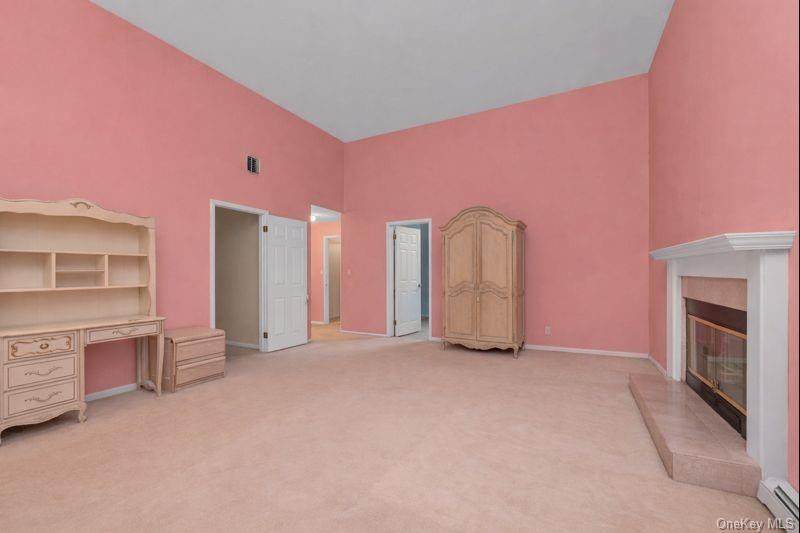 39 Fleets Cove Road Huntington, NY 11743 - Photo 12 of 20 Unfurnished bedroom with high vaulted ceiling, light carpet, baseboard heating, a glass covered fireplace, and an office area