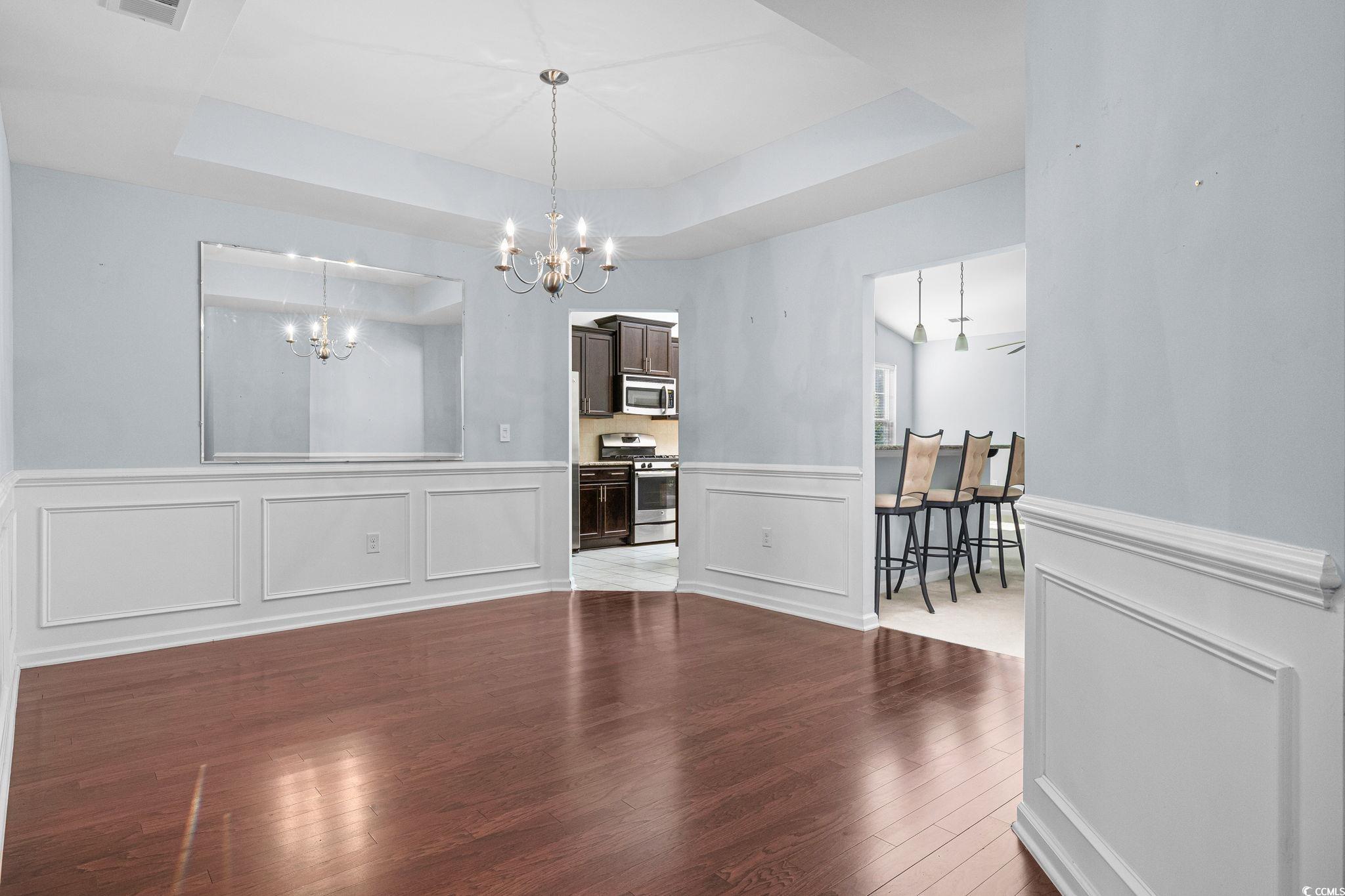 817 Arezzo Way, Unit 1001 Myrtle Beach, SC 29579 - Photo 6 of 40 Dining area with a raised ceiling, dark wood-type flooring, a decorative wall, a wainscoted wall, and a chandelier