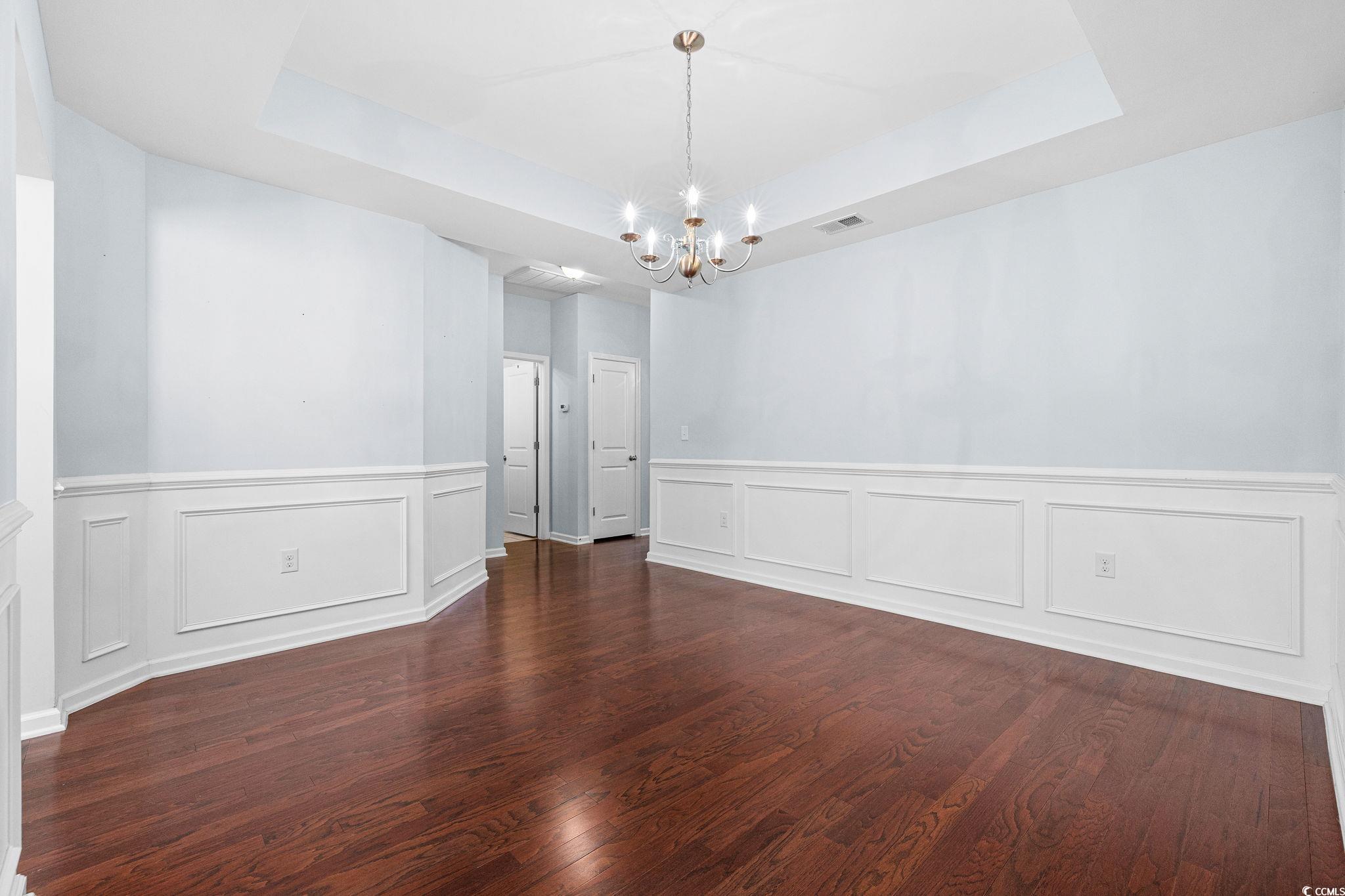 817 Arezzo Way, Unit 1001 Myrtle Beach, SC 29579 - Photo 8 of 40 Unfurnished dining area featuring a raised ceiling, dark wood-style flooring, a chandelier, wainscoting, and a decorative wall